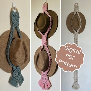 Peut inclure: Trois porte-chapeaux en macramé avec des cordons de différentes couleurs. Les porte-chapeaux sont faits avec un motif de nœuds et ont un pompon en bas. Les porte-chapeaux sont suspendus à un crochet sur un mur blanc. Le texte "Modèle PDF numérique" est sur un cercle brun dans l'image.