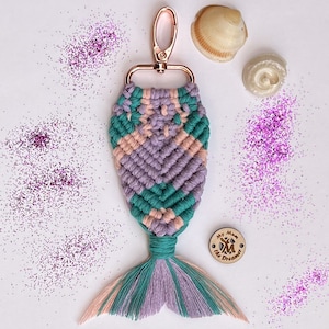 K&ouml;nnte beinhalten: Ein pinkfarbener, gr&uuml;ner und violetter Schl&uuml;sselanh&auml;nger in Form einer Meerjungfrauenflosse mit einem Holzanh&auml;nger, auf dem "My Mum the Dreamer" steht. Der Schl&uuml;sselanh&auml;nger ist von pinkfarbenem Glitzer umgeben.