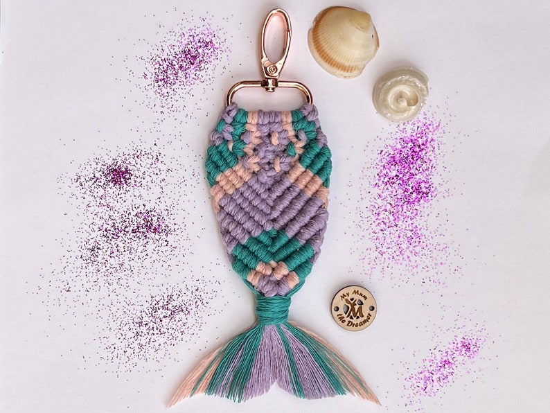 K&ouml;nnte beinhalten: Ein pinkfarbener, gr&uuml;ner und violetter Schl&uuml;sselanh&auml;nger in Form einer Meerjungfrauenflosse mit einem Holzanh&auml;nger, auf dem "My Mum the Dreamer" steht. Der Schl&uuml;sselanh&auml;nger ist von pinkfarbenem Glitzer umgeben.
