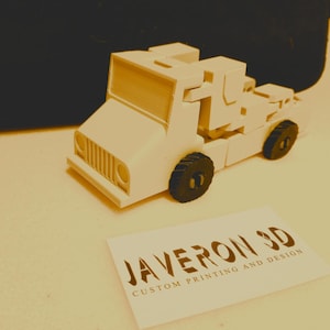 Pode incluir: Um caminhão de brinquedo branco impresso em 3D com rodas pretas. O caminhão é um design personalizado e tem as palavras "JAVERON 3D IMPRESSÃO E DESIGN PERSONALIZADO" impressas em um cartão branco na frente dele.