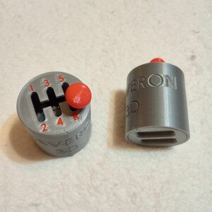 May include: Two gray 3D printed gear shift knobs with red buttons. The knobs are labeled "VERON 3D". One knob has a gear shift pattern with numbers 1 through 5 and "R" for reverse.