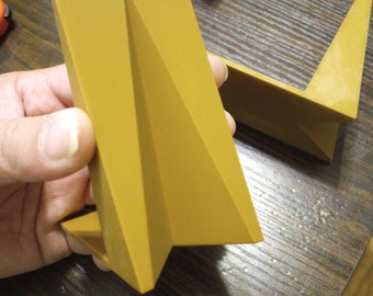 May include: A gold-coloured, geometric, paper-like stand with a triangular shape. The stand is made of a thick, sturdy material and has a smooth, glossy finish.