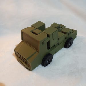 Pode incluir: Um caminhão de brinquedo verde com rodas pretas. O caminhão é feito de plástico e tem um design simples.