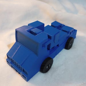 Pode incluir: Um caminhão de brinquedo azul com rodas pretas. O caminhão é feito de plástico e tem um design simples.
