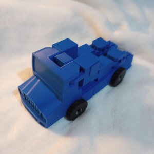 Pode incluir: Um caminhão de brinquedo azul feito de blocos de encaixe. O caminhão tem quatro rodas e uma grade frontal detalhada.
