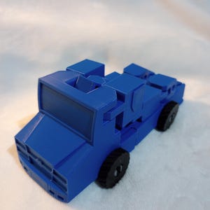 Pode incluir: Um caminhão de brinquedo azul com rodas pretas. O caminhão é feito de plástico e tem um design simples.