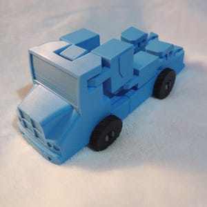 Pode incluir: Um caminhão de brinquedo de plástico azul com rodas pretas. O caminhão é feito de blocos que se encaixam e pode ser montado de diferentes maneiras.