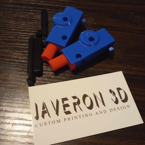 May include: Two blue and orange 3D-printed components with black rods, and a business card. The card reads "JAVERON 3D CUSTOM PRINTING AND DESIGN" in a stylized font. The components have a mechanical design.