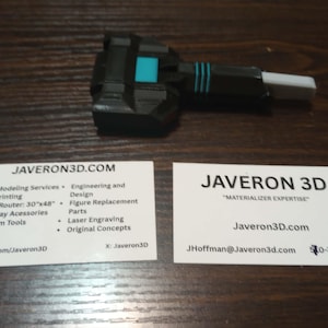 Puede incluir: Un componente mecánico negro, azul y blanco con una base rectangular y una punta blanca que sobresale, acompañado de dos tarjetas de visita blancas con el texto JAVERON3D.COM, JAVERON 3D y varias descripciones de servicios.