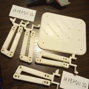 Op de afbeelding: Een set witte kunststof onderdelen voor het bouwen van een model. De onderdelen omvatten een basis, armen en benen. De onderdelen zijn gelabeld met "JAVERON 3D CUSTOM PRINTING AND DESIGN".