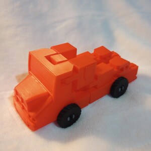 Pode incluir: Um caminhão de bombeiros de brinquedo laranja brilhante feito de blocos de plástico. O caminhão tem rodas pretas e um design detalhado.