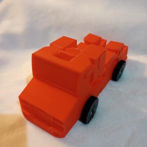 Pode incluir: Um caminhão de bombeiros de brinquedo vermelho feito de blocos. O caminhão tem rodas pretas e uma escada na parte de trás.