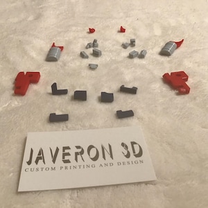 Puede incluir: Surtido de pequeñas piezas impresas en 3D en rojo, gris y negro. Las piezas están dispuestas sobre una superficie blanca. El texto "JAVERON 3D IMPRESIÓN Y DISEÑO PERSONALIZADOS" está impreso en una tarjeta blanca.