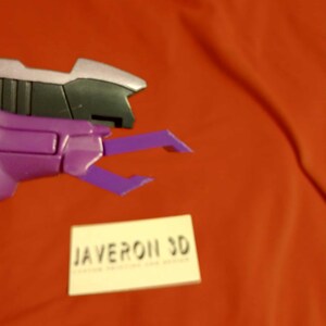 May include: A close-up of a purple and black mechanical claw on a red background. The claw has a silver accent and is labeled "JAVERON 3D" in white text on a small white rectangle.