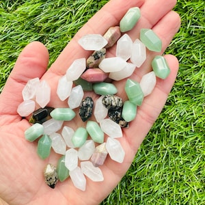 Puede incluir: Una colección de puntas de piedras preciosas de varios colores en una mano. Las puntas son de color verde, blanco y rosa. Las puntas son todas de aproximadamente el mismo tamaño y forma.