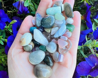 以下が含まれることがあります： 手の中に、緑、青、ピンク、白など、さまざまな色の小さな研磨された石が握られています。