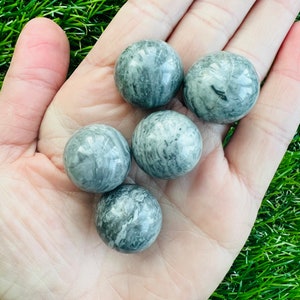 May include: Five smooth, grey and white marble spheres, each with a unique swirling pattern, are displayed in a hand.