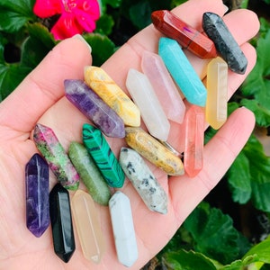 May include: A collection of 16 different coloured crystal points, including amethyst, rose quartz, clear quartz, and green aventurine. The points are arranged in a hand, with the tips pointing upwards.