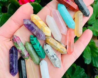 May include: A collection of 16 different colored crystal points, including amethyst, rose quartz, clear quartz, and green aventurine. The points are arranged in a hand, with the tips pointing upwards.