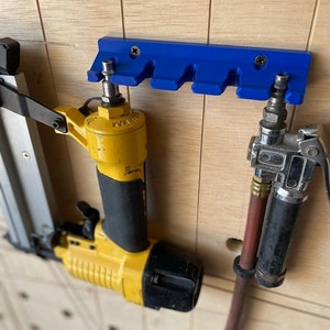 May include: A blue plastic wall-mounted tool holder with five slots, holding a yellow and black air nailer and a silver air compressor with a brown hose.