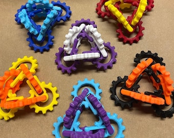 Op de afbeelding: Zes driehoekige, in elkaar grijpende tandwielspeelgoed in verschillende kleuren: blauw, wit, paars, oranje, zwart en rood. Elk tandwiel is gemaakt van plastic en heeft een unieke kleur.