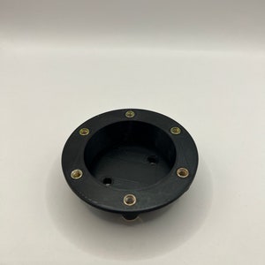 May include: Black plastic round base with eight gold screws around the edge. The base has a circular opening in the center.