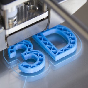 May include: A 3D printer creating a blue plastic model of the letters "3D".