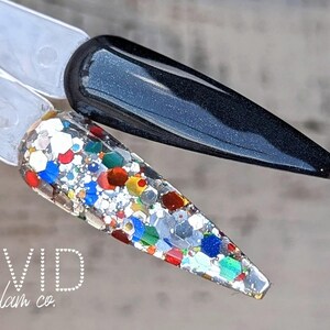 Könnte beinhalten: Zwei Nagellackmuster. Eines ist glänzend schwarz, das andere ist transparent mit bunten Glitzer. Der Text "VIVID glam co." befindet sich unten. Die Nagellackmuster befinden sich auf einer hellbraunen Oberfläche.