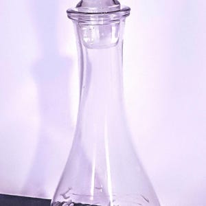 May include: A clear glass decanter with a stopper. The decanter has an etched design of grapes and vines.
