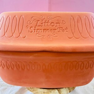 May include: A terracotta-colored Litton Simmer Pot with a lid. The pot features decorative spiral and dotted patterns around the rim and lid. The text "Litton Simmer Pot" is embossed on the lid.