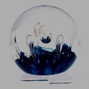 May include: A clear glass paperweight with a blue and white swirl design inside. The swirl is reminiscent of a wave or a cloud.