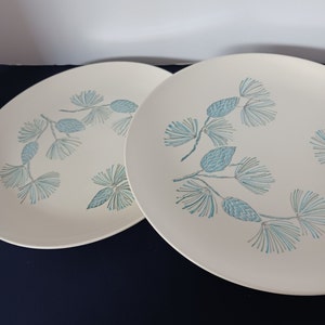 May include: Two white ceramic dinner plates with a blue and green pine cone design.