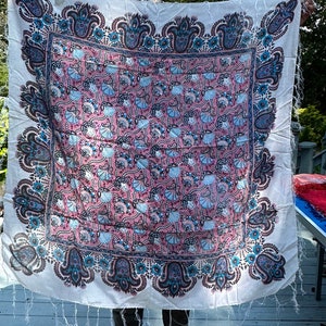 May include: A white cotton scarf with a pink, blue, and black paisley pattern. The scarf has a fringed edge.