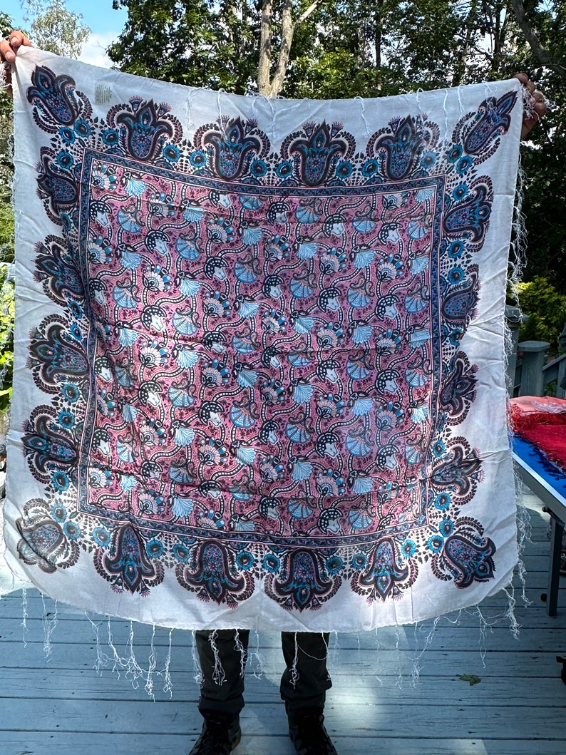 May include: A white cotton scarf with a pink, blue, and black paisley pattern. The scarf has a fringed edge.