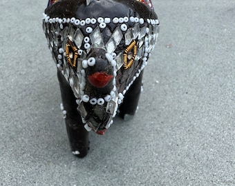 May include: A small black elephant figurine decorated with colorful mosaic tiles and white beads. The elephant's head is adorned with red and gold accents.