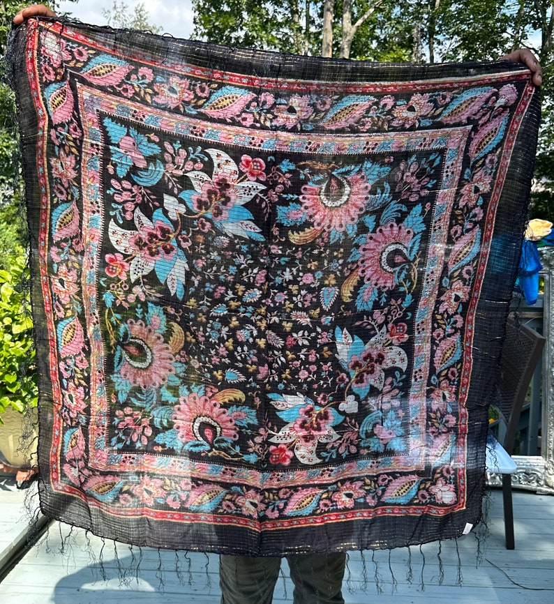 May include: A black silk scarf with a floral pattern in shades of pink, blue, and gold. The scarf has a fringed edge and is made of a lightweight fabric.