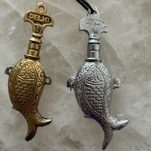 May include: Two silver and gold fish-shaped bottle stoppers with ornate designs. The stoppers have a loop at the top for hanging and are labeled "DELHI" and "INDIA".