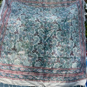 May include: A white cotton throw blanket with a paisley pattern in shades of blue, green, and red. The blanket has a fringe border and is woven with a grid pattern.