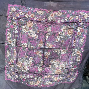 May include: A dark purple shawl with a floral pattern in shades of pink, brown, and blue. The shawl has a fringed edge.