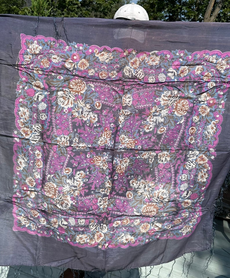 May include: A dark purple shawl with a floral pattern in shades of pink, brown, and blue. The shawl has a fringed edge.