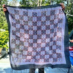 May include: A black silk scarf with a checkered pattern in shades of purple, brown, and white. The scarf has a fringe border.