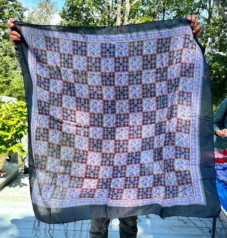 May include: A black silk scarf with a checkered pattern in shades of purple, brown, and white. The scarf has a fringe border.