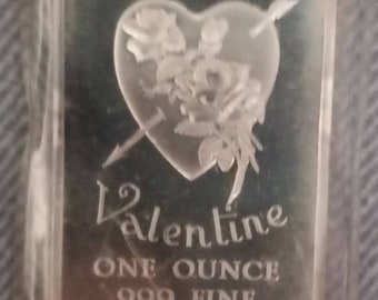 May include: Silver bullion bar with a heart and arrow design. The bar reads "Be my Valentine, One Ounce .999 Fine Silver, 14 February 1973".