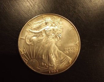 Könnte beinhalten: Eine silberne American Eagle Münze mit dem Bild von Lady Liberty auf der Vorderseite. Die Münze trägt die Inschrift "In God We Trust" und das Jahr "1994".