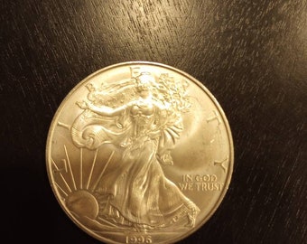 Könnte beinhalten: Silberne American Eagle Münze mit einer Darstellung von Lady Liberty, die nach vorne geht und in ihrer rechten Hand einen Zweig mit Olivenblättern und in ihrer linken Hand eine Fackel hält. Die Münze trägt die Inschrift "In God We Trust" und das Jahr "1996".
