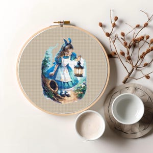 May include: A cross-stitch embroidery hoop featuring Alice from Alice in Wonderland holding a lantern. The background is a woodland scene with a tree stump and flowers. The embroidery is worked in shades of blue, green, and brown.