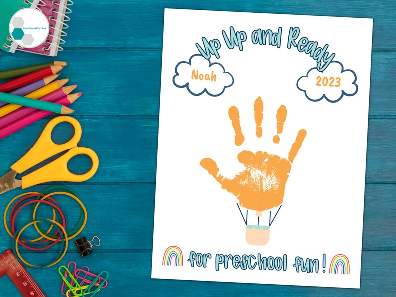 May include: A printable handprint art activity for preschoolers. The design features a hot air balloon with a handprint as the balloon, a blue and white cloud with the text "Noah" and another blue and white cloud with the text "2023". The text "Up Up and Ready for preschool fun!" is below the balloon.
