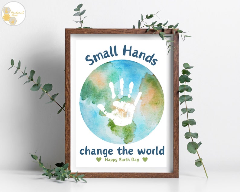 May include: A framed print with a watercolor painting of the Earth with a white handprint in the center. The text "Small Hands change the world" is written in blue below the Earth. The text "Happy Earth Day" is written in green below the blue text.