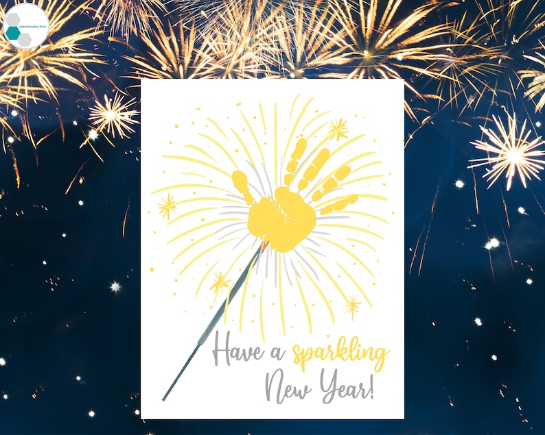 May include: A white card with a yellow handprint in the center, surrounded by yellow lines radiating outward, resembling fireworks. The text "Have a sparkling New Year!" is written below the handprint.
