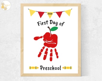 May include: A framed print featuring the text First Day of Preschool with the year 2026. The design includes a red handprint shaped like an apple with a green leaf, a yellow and red bunting banner at the top, and yellow crayon icons on the sides.